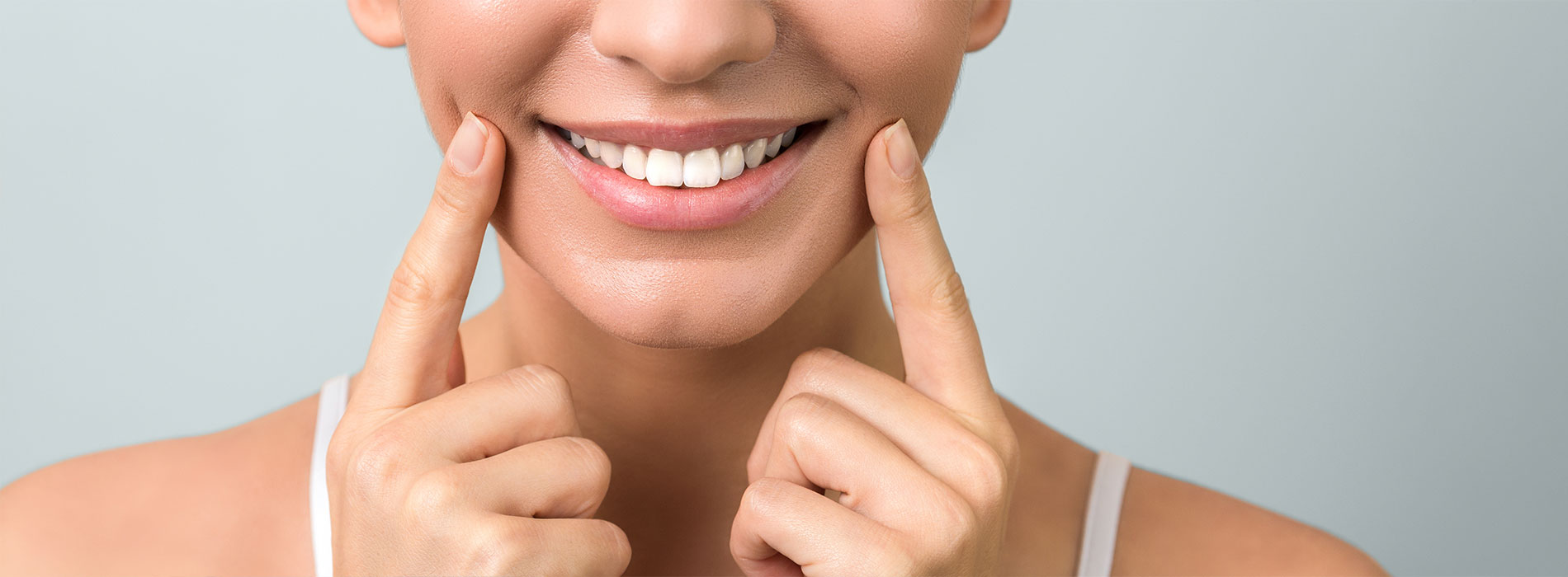 A woman with a radiant smile, looking directly at the camera with her hand gently placed on her face.