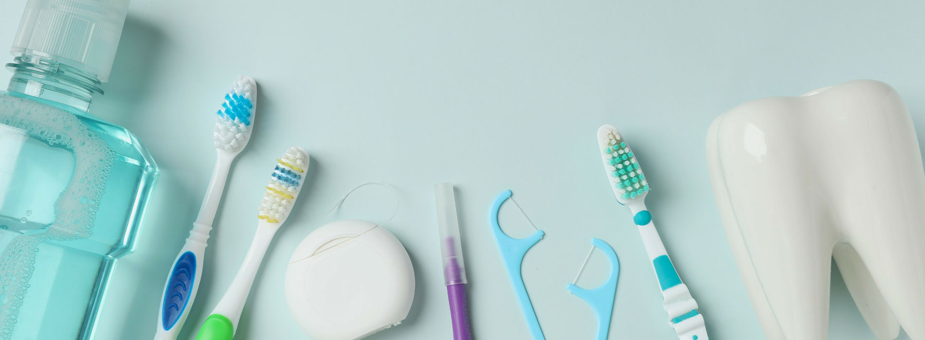 The image displays a collection of oral hygiene items such as toothbrushes, toothpaste, dental floss, and mouthwash arranged on a light blue background with a teal border, suggesting a focus on dental care.