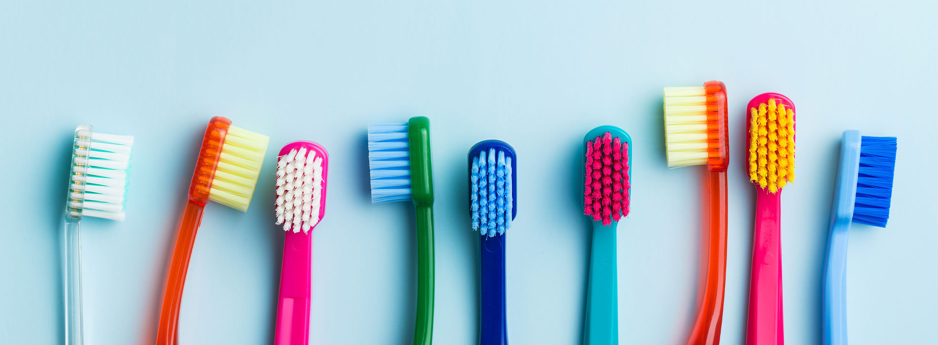 The image displays a collection of colorful toothbrushes with different bristle patterns, arranged neatly against a plain background.