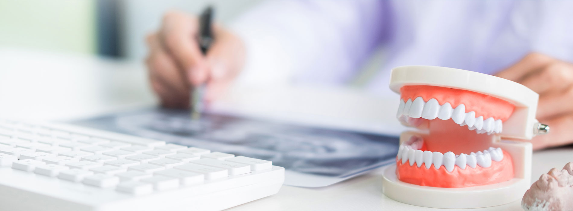 An image showing a person writing on a computer screen with a dental model and keyboard in the foreground.