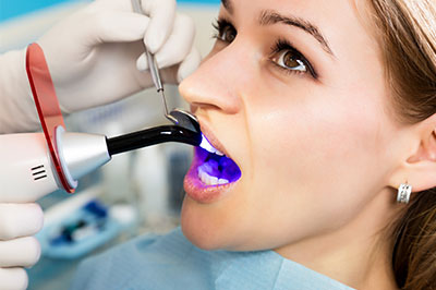 An individual receiving dental treatment with a purple light device, possibly an LED light for curing resin in dental procedures.