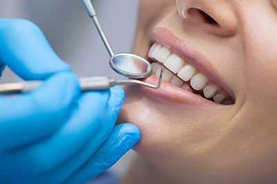 The image shows a dental professional performing oral care on a patient s teeth while wearing protective gloves and using dental tools.