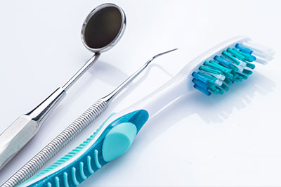 The image shows a collection of dental tools, including a toothbrush with blue bristles, a scaler, and a pair of scissors, arranged on a white surface next to a dental mirror.